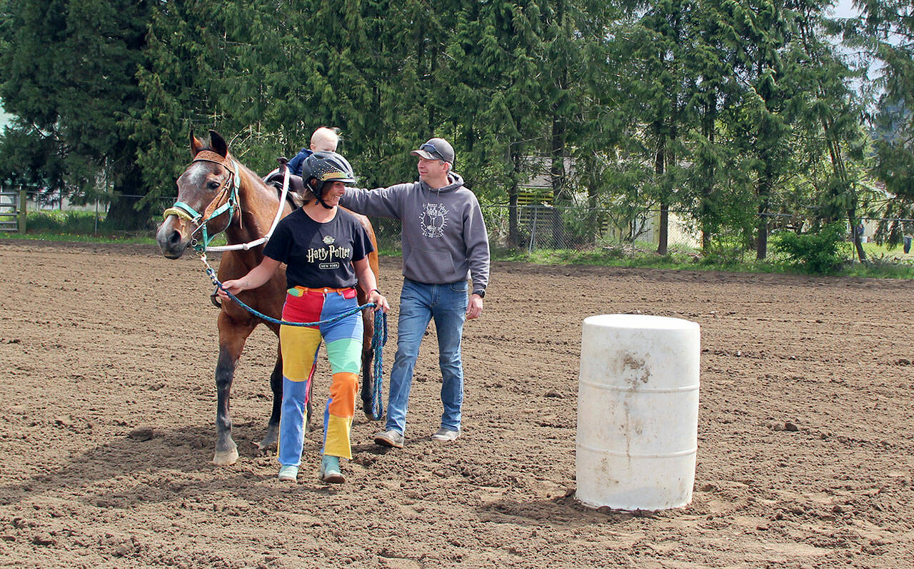 At a May 6 Patterned Speed Horse game show honoring his great-grandfather Ted Crosby, a very young Nyle Crosby James is led through his first competitive barrel racing pattern by his mother, Ady Crosby, while steadied by his father Jeff James. Ted Crosby, 87, passed away March 30 of complications of prostate cancer. (Karen Griffiths/For Peninsula Daily News)