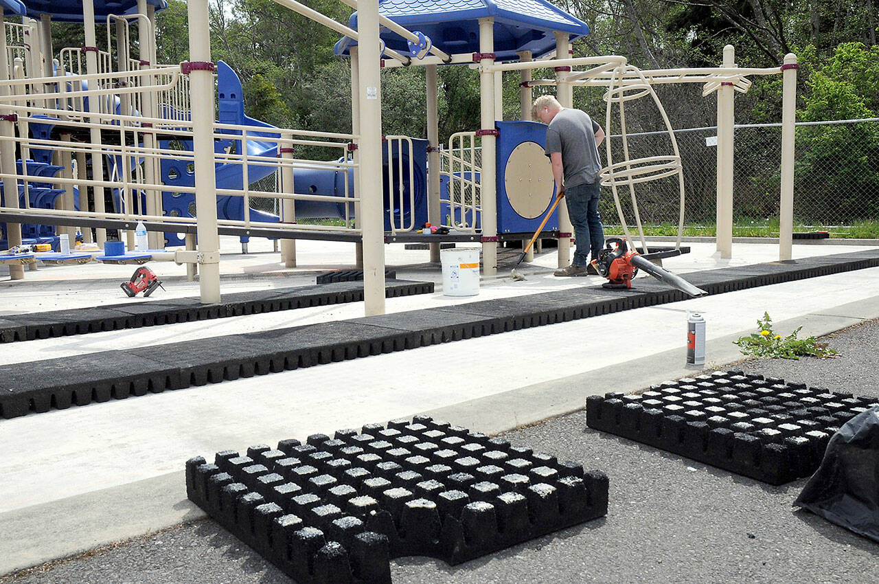 Riley Peterson of R & R Construction of Carbonado applies adhesive to the concrete base surrounding the playground equipment at Shane Park on Tuesday in Port Angeles in preparation for the replacement of cushioned tiles that make up the play surface. (KEITH THORPE/PENINSULA DAILY NEWS)