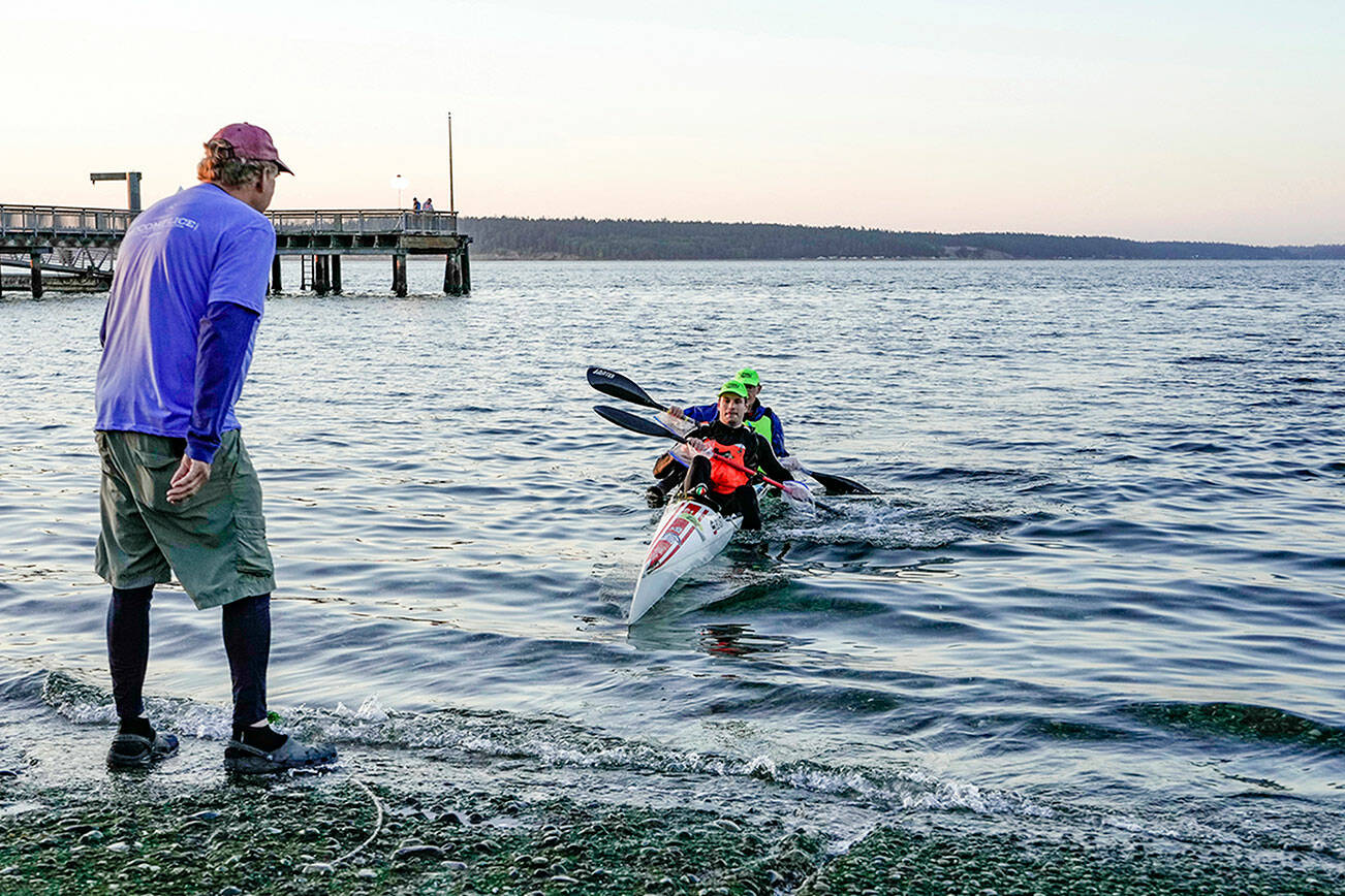 Northwest Maritime Center volunteer Brad Bebout, left, stands ready to assist team Beasts From the East, Ivan Medvedev and Egor Klevak, front, both from Seattle, as they finish first the 70-mile paddle from Tacoma to Port Townsend on Saturday morning. (Steve Mullensky/for Peninsula Daily News)