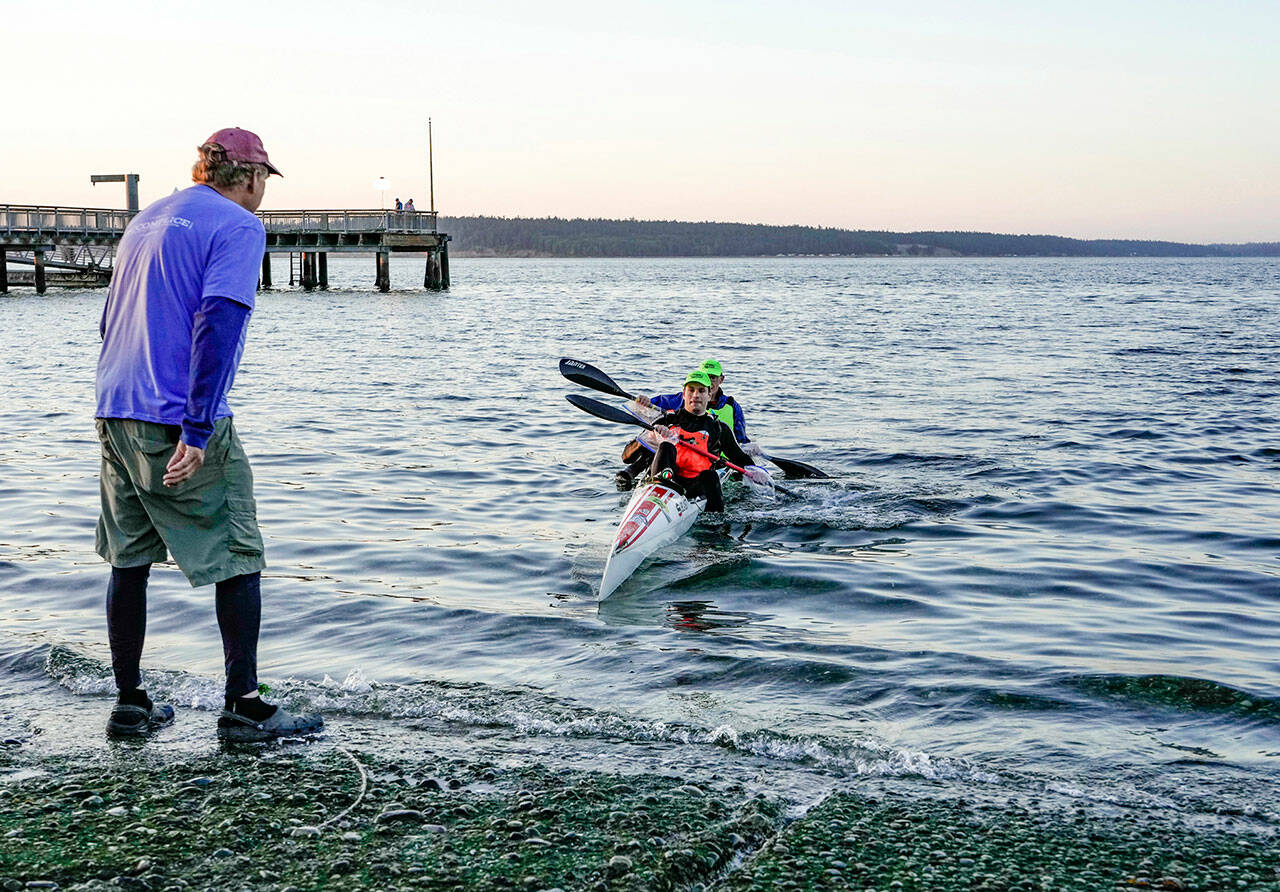 Northwest Maritime Center volunteer Brad Bebout, left, stands ready to assist team Beasts From the East, Ivan Medvedev and Egor Klevak, front, both from Seattle, as they finish first the 70-mile paddle from Tacoma to Port Townsend on Saturday morning. (Steve Mullensky/for Peninsula Daily News)