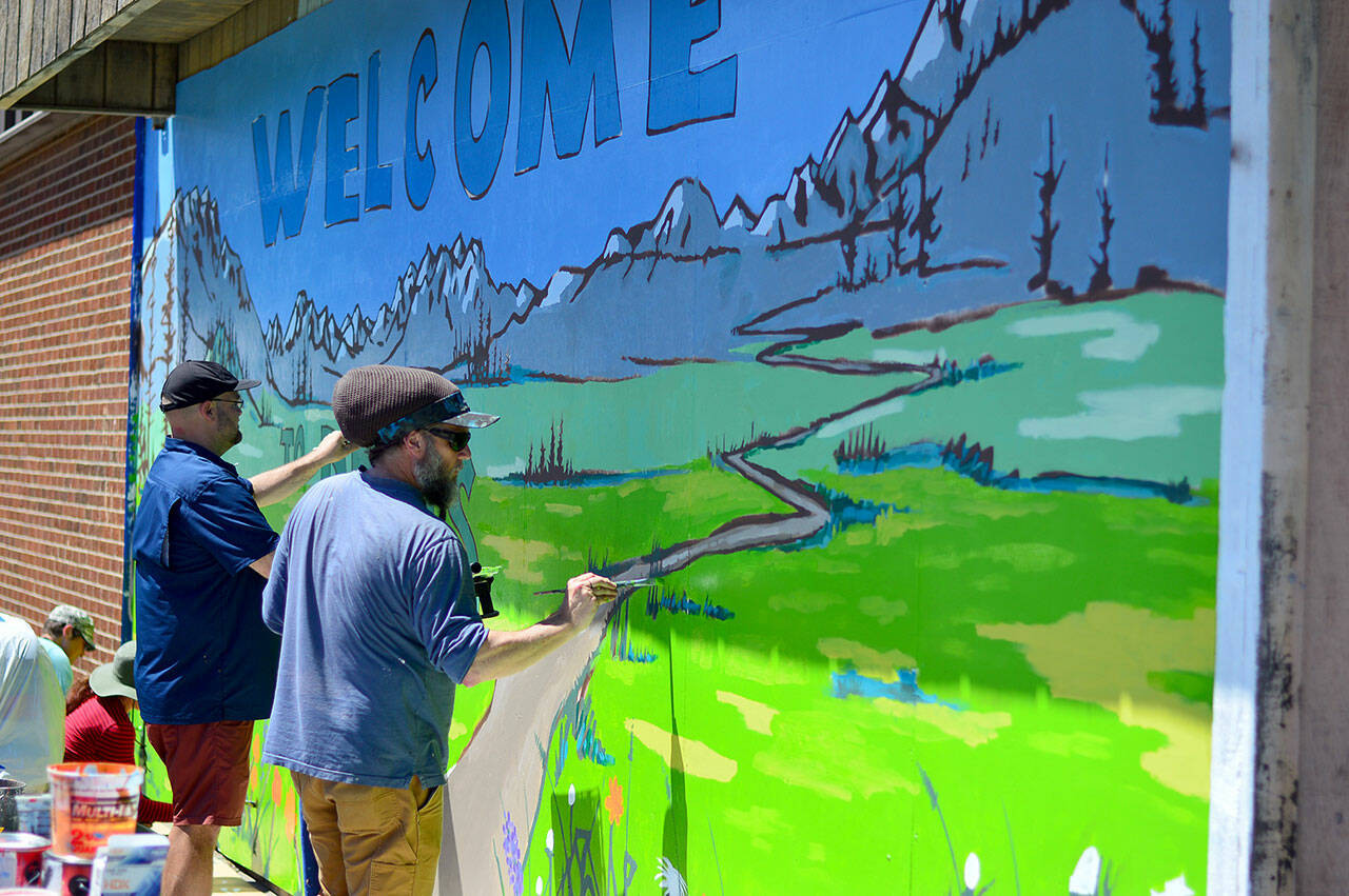 In a PT Artscape project, Blue Heron Middle School teacher Charlie Fornia, left, and artist Jesse Watson finish painting a “Welcome to PTHS” mural on the woodshop building at Port Townsend High School. PT Artscape hired Watson to design the mural and hosted a morning of painting with elementary, middle school and high school students from around Port Townsend. (Diane Urbani de la Paz/for Peninsula Daily News)