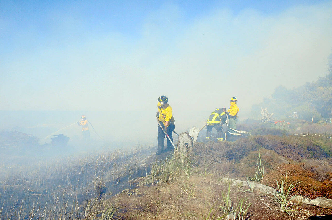 Clallam County Fire District 2 firefighters, with assistance from surrounding districts, work to extinguish fire of beach logs and grasses that scorched a stretch of beach along the Strait of Juan de Fuca at the north end of Four Seasons Ranch and threatened numerous homes on Saturday. (Keith Thorpe/Peninsula Daily News)
