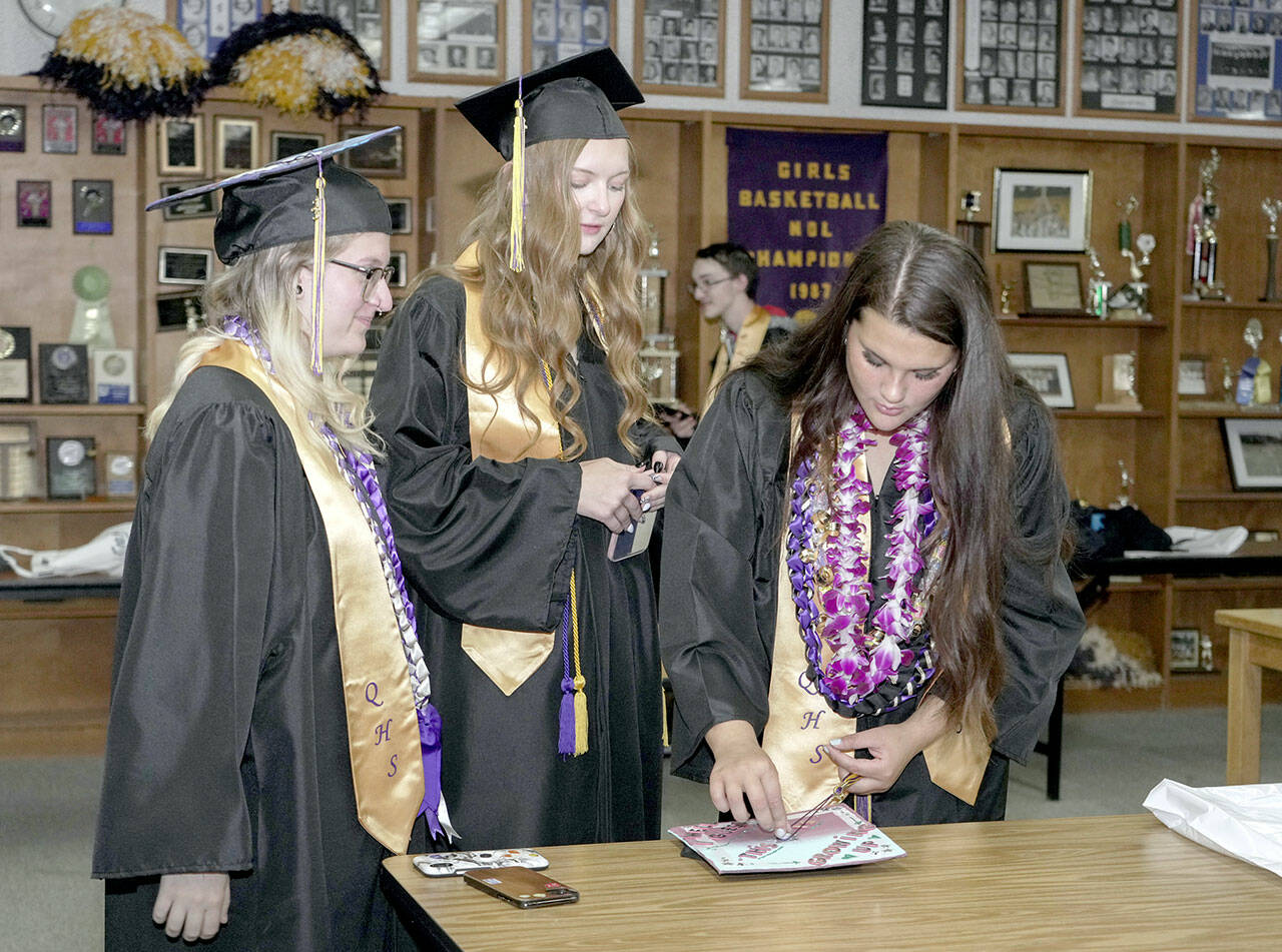 Quilcene High School graduate Rhiannon Chapman, right, puts the finishing touches on her mortar board while Ashley Jones, center, and Zoey Carver, left, watch. The trio were waiting for their graduation ceremony to start on Saturday at the high school. (Steve Mullensky/for Peninsula Daily News)