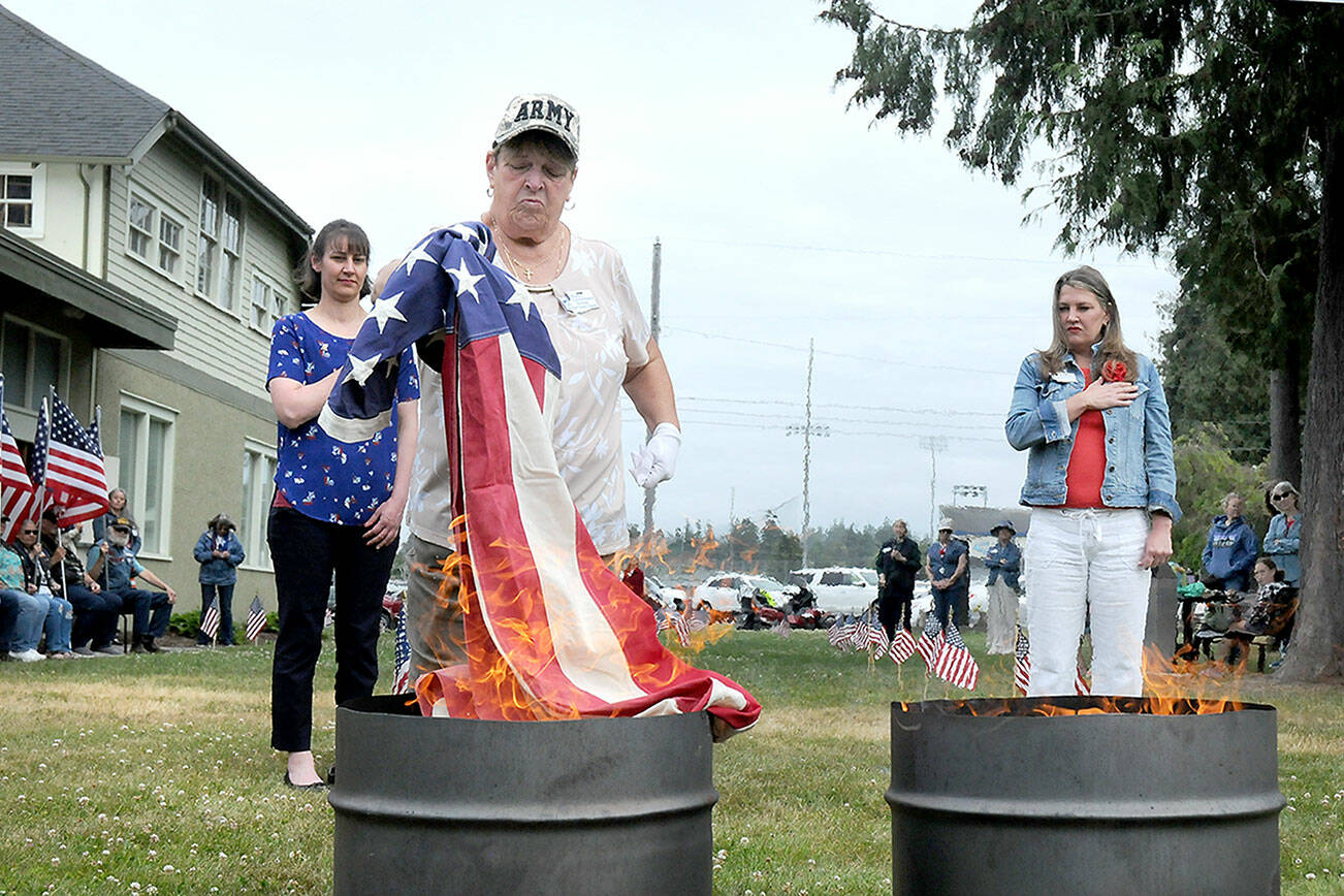 U.S. Army veteran Nancy Zimmerman, a member of the Michael Trebert Chapter of the Daughters of the American Revolution, is flanked by fellow DAR members Amira-Lee Salavati, left, and Lindsey Christianson as Zimmerman incinerates a used American Flag during a flag retirement ceremony on Wednesday at the Northwest Veterans Resource Center in Port Angeles. A total of 24 cotton flags were burned during the Flag Day ceremony. (Keith Thorpe/Peninsula Daily News)