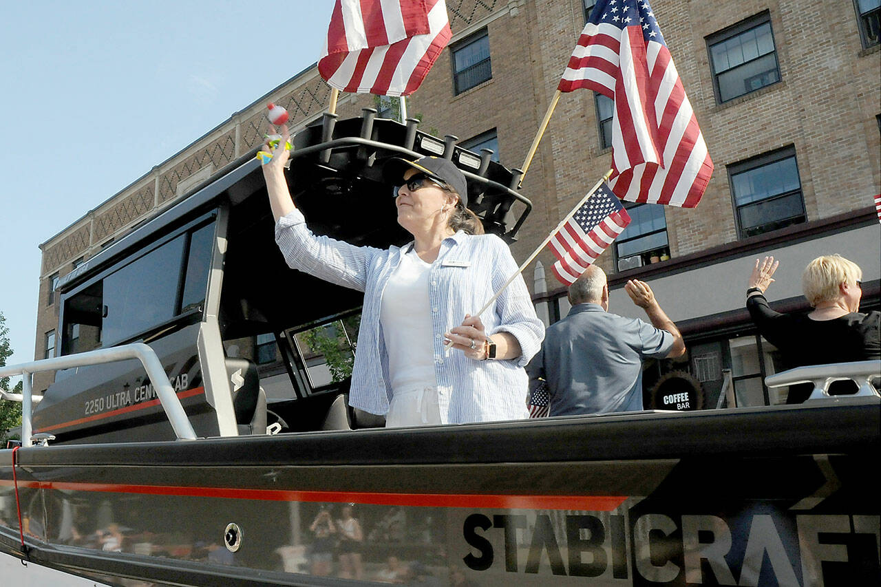 Port of Port Angeles Commissioner Colleen McAleer prepares to toss goodies to the crowd from the back of a trailered boat during Tuesday’s Independence Day parade in Port Angeles. McAleer, along with fellow commissioners Steve Burke and Connie Beauvais, facing the other side, were the parade’s grand marshals in honor of the 100th anniversary of the port. (Keith Thorpe/Peninsula Daily News)