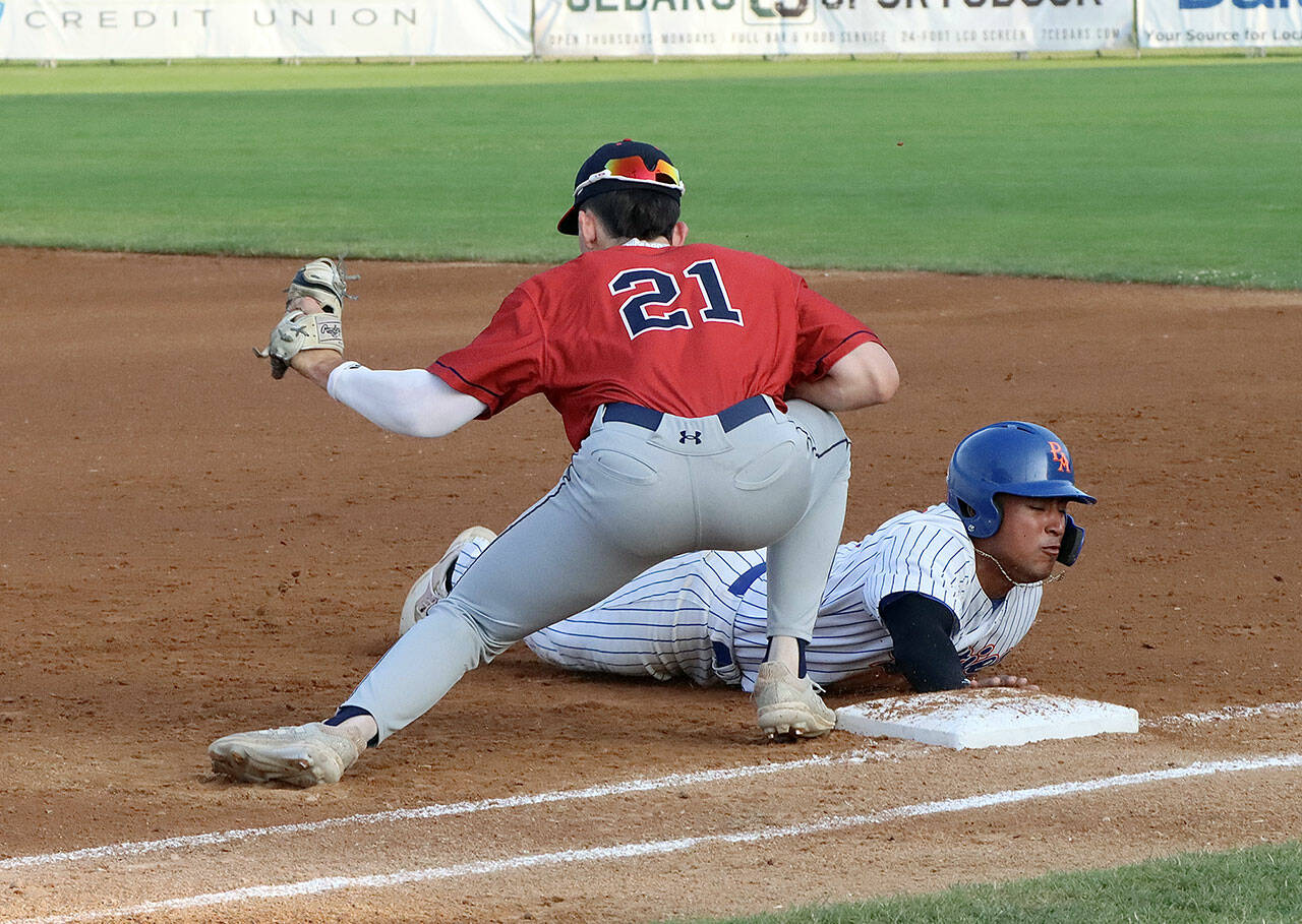 Port Angeles’ Roberto Nunez III slides safely back to first base as Wenatchee’s Easton Amundson is a tad late with the tag on the throw from the pitcher. (Dave Logan/for Peninsula Daily News)