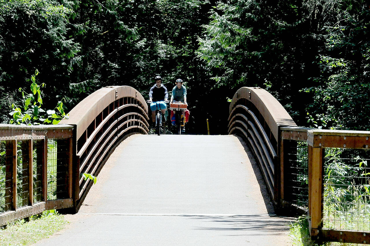 Tom Rooney of Seattle, left, and Marie Cazanave of Montreal, Quebec ride their bicycles over a 201-foot long footbridge spanning a small creek on Thursday at Sequim Bay State Park east of Sequim. (KEITH THORPE/PENINSULA DAILY NEWS)