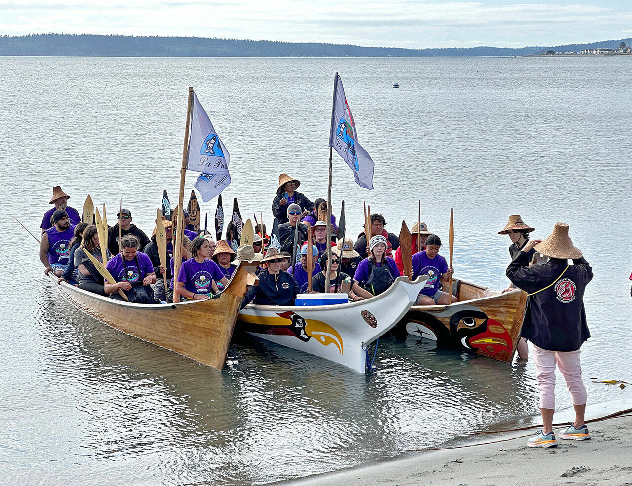 Celeste Dybeck, elder with the Jamestown S’Klallam Tribe in Sequim, invites the pullers from the Quileute Tribe in La Push to come ashore at Fort Worden in Port Townsend and rest and eat before continuing the Paddle to Muckleshoot for the annual Tribal Canoe Journey. The tribal members are wearing purple, the color of the Missing and Murdered Indigenous Women and Children movement, to honor the memory of tribal member Virginia Castaneda, 19, who was murdered in a domestic violence dispute about six years ago. An empty seat was left for her in one of the canoes. The stop was the final one on the North Olympic Peninsula before canoes are due to reach their destination on Sunday. (Steve Mullensky/for Peninsula Daily News)