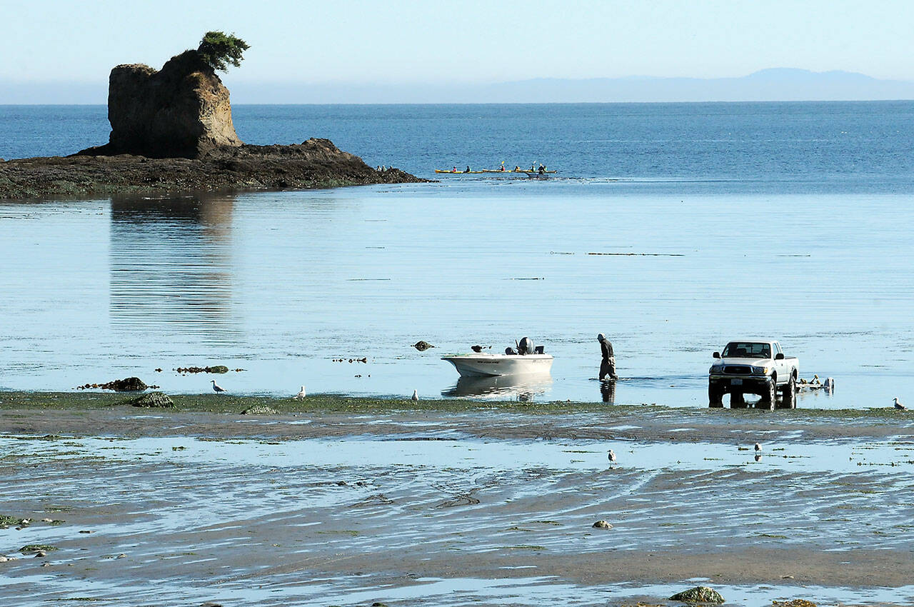 Greg Holmquist of Port Angeles walks to his beached boat to pull it to a waiting trailer, parked more than 100 yards from the end of the regular boat ramp as a group of kayakers paddle around the Bachelor Rock sea stack during Thursday’s minus-2 low tide at Freshwater Bay west of Port Angeles. Holmquist said it was a perfect day for boating with calm seas and pleasant weather. (Keith Thorpe/Peninsula Daily News)