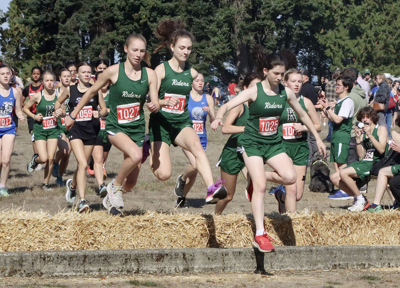 Port Angeles' Leia Larson, Faerin Tate and Miriam Cobb jump over the hay bales at the start of the 45th annual Salt Creek Invitational at Salt Creek County Park on Saturday. Larson and Cobb both finished in the to 10 while all three Roughriders finished in the top 20. (Dave Logan/for Peninsula Daily News)