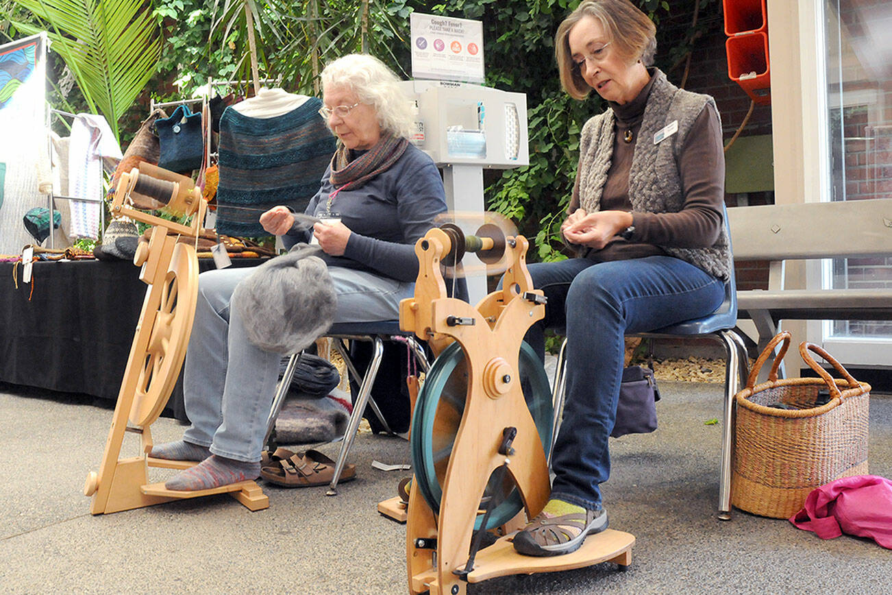 Janice Dotson of Port Angeles, left, and Karen Turner of Sequim, both members of the North Olympic Shuttle & Spindle Guild, pull yarn on spinning wheels as part of a demonstration of the art during the Pacific Northwest Fiber Exposition on Saturday at Vern Burton Community Center in Port Angeles. The three-day expo featured workshops, demonstrations and a marketplace of yarns and fibers. (Keith Thorpe/Peninsula Daily News)