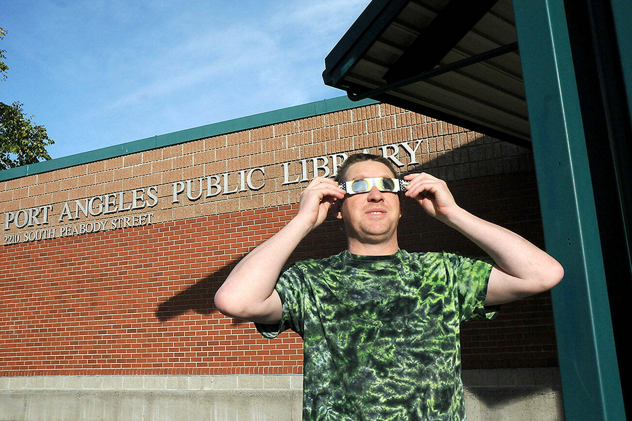 Jeff Clark, facilities technician for the North Olympic Library System, wears special glasses to observe Saturday’s partial eclipse of the sun in front of the Port Angeles Public Library. The annular eclipse was visible as a “ring of fire” for a swath of watchers across Oregon to Texas and Mexico, was visible on the North Olympic Peninsula at about 80 percent with a large portion of the solar disc obscured by the Moon. (Keith Thorpe/Peninsula Daily News)