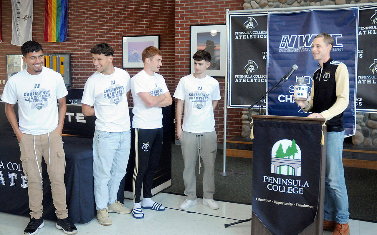 Peninsula College men’s soccer coach Jake Hughes, right, holds a gag “swear jar” poking fun of player Nil Grau, who used a number of swear words during an exuberant live-streamed postgame interview on Sunday after the team defeated Highline in the NWAC championship match on Sunday in Tukwila. The team was honored by the school at the Pirate Union Building on Tuesday. Next to the podium are players, from left, Manny Garcia, Konrad Muller, Pip van der Ende and Alfie Tucker. (Keith Thorpe/Peninsula Daily News)