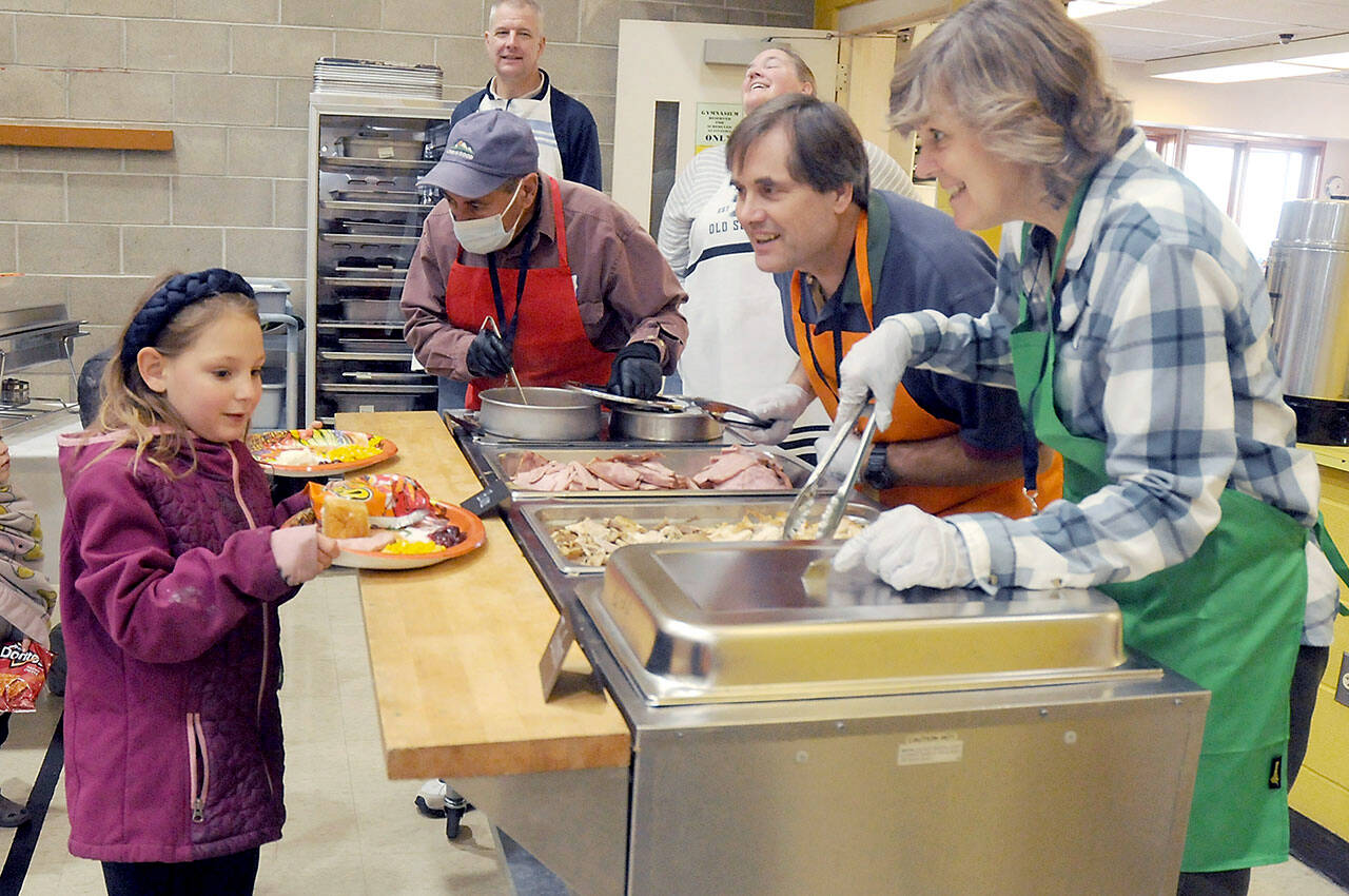 Anna-Marie Tax, 7, of Port Angeles and her brother A.J. Tax, 4, behind, are served by volunteers, from left, Phil Becillis, Lorenz Sololmann and Patty Sollman during Thursday’s Community Dinner at Queen of Angeles community hall in Port Angeles. Hundreds of people took part in the free meal, which featured traditional Thanksgiving fare, dessert and the companionship of other community members. (Keith Thorpe/Peninsula Daily News)