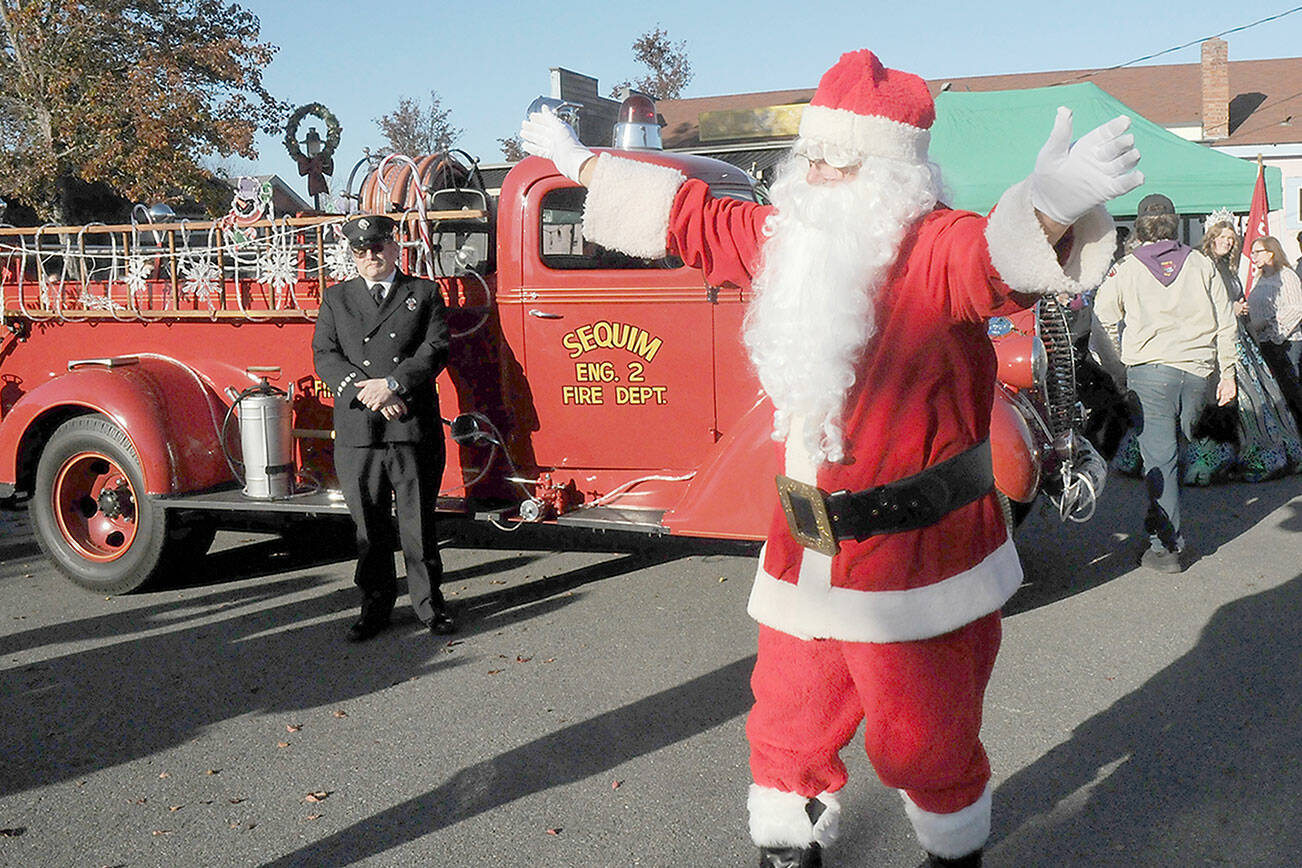 Santa Claus, portrayed by Stephen Rosales of Sequim, waves to the crowd after his arrival by vintage fire truck at Centennial Place in downtown Sequim on Saturday, part of the city’s Hometown Holidays celebration. Santa, accompanied by Irrigation Festival royalty, greeted children next to the city’s Christmas tree in an event that also featured music by the Sequim City Band and a lighted tractor parade. (Keith Thorpe/Peninsula Daily News)