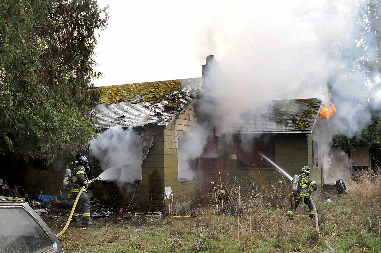 Port Angeles firefighter Ryan Gosling, left, and Samantha Harik work to extinguish a blaze at an unoccupied house at 1338 W. Lauridsen Blvd. on the edge of Port Angeles on Saturday. (Keith Thorpe/Peninsula Daily News)