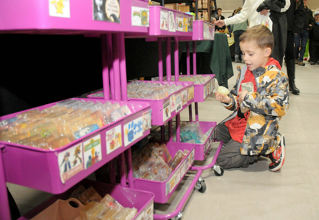 Enzo Ramirez, 4, of Port Angeles clutches his dollar bill while searching for an affordable gift to purchase at a vendor table set up by Port Angeles-based Power Up Perler & Soaps during Saturday’s Holiday Market at Vern Burton Community Center in Port Angeles. The market featured dozens of gift and craft tables by local artisans, including a donation and craft table benefiting Peninsula Friends of Animals. (Keith Thorpe/Peninsula Daily News)