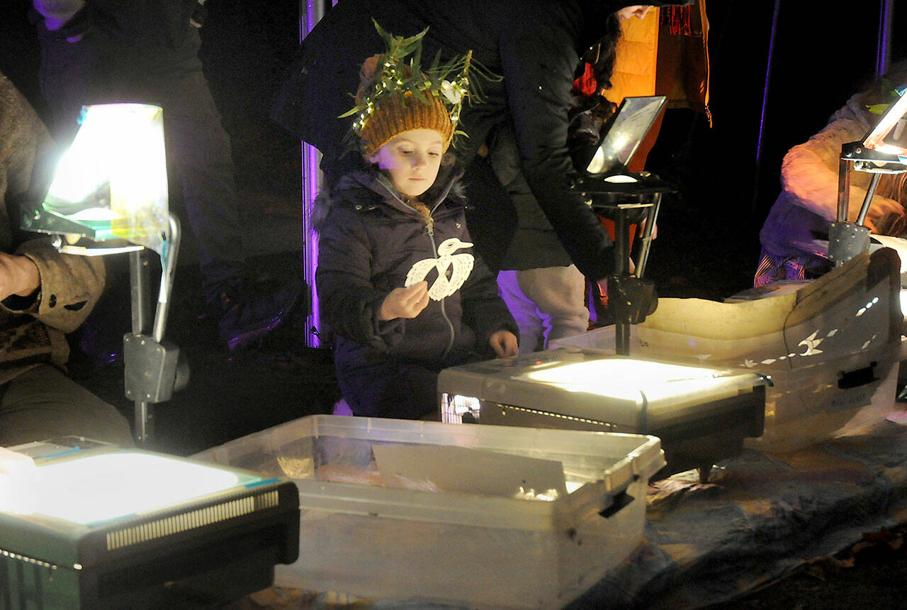 Farrah Friswold, 5, of Port Angeles looks at a silhouette of a bird for placement on an overhead projector at an interactive light station at Wintertide on Saturday in Webster’s Woods Sculpture Park at the Port Angeles Fine Arts Center. The Wintertide Festival of Lights featured a variety of hands-on activities, food, music, a fire dancing exhibition, a lantern walk and a seasonal selection of illuminated sculptures, as well as an ongoing Makers Market of artistic gifts in the fine art center gallery. (Keith Thorpe/Peninsula Daily News)