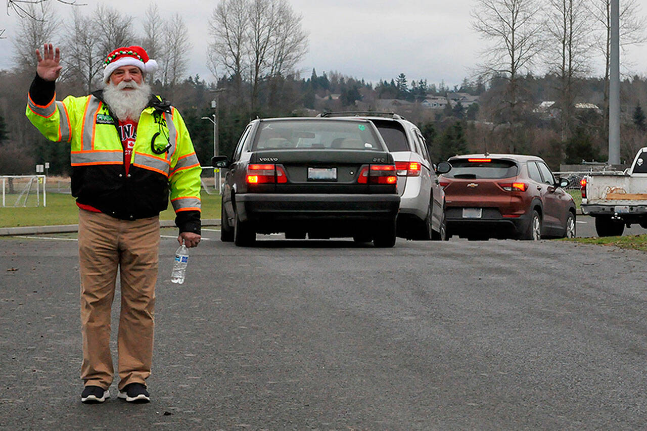 Butch Zaharias, a captain and division chief with the Community Emergency Response Team (CERT), checks in on drivers and fellow CERT members in festive garb during the Family Holiday Meal Bag distribution in Sequim’s Carrie Blake Park. (Matthew Nash/Olympic Peninsula News Group)