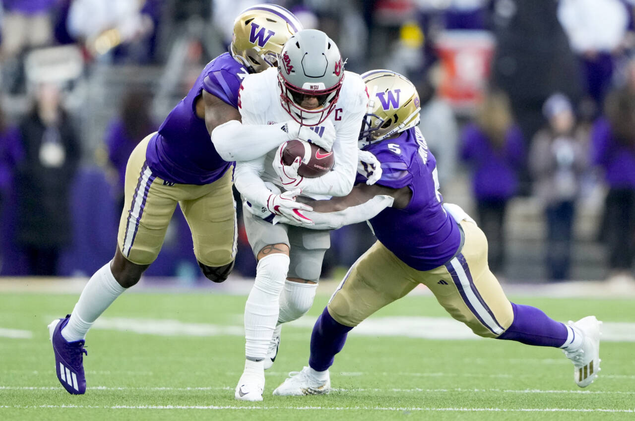 Washington State wide receiver Lincoln Victor (5) is tackled by Washington cornerback Dominique Hampton, left, and linebacker Edefuan Ulofoshio, right, during the Apple Cup on Nov. 25 in Seattle. Washington and Washington State will continue to play each other in football for at least another five years, but the Apple Cup will no longer be a conference game. (Lindsey Wasson/The Associated Press)