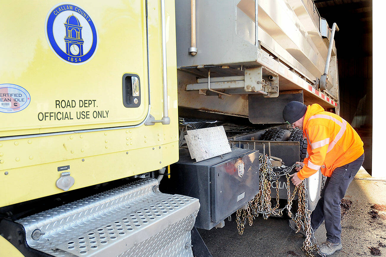 Clallam County Road Department maintenance worker Jeremy Reeves loads a set of tire chains onto a county sand truck on Wednesday at the county shop in Port Angeles in preparation for potential snow on the North Olympic Peninsula. (Keith Thorpe/Peninsula Daily News)