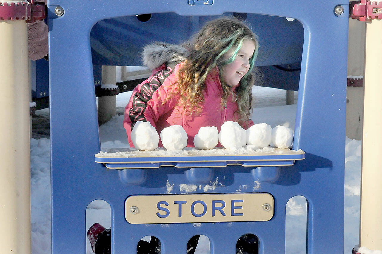 Madrona Villella, 7, of Port Angeles looks out from a pretend storefront lined with snowballs at the children’s playground at Shane Park on a chilly Friday in Port Angeles. The youngster braved single-digit wind chills for a chance at a snow day in the park. (KEITH THORPE/PENINSULA DAILY NEWS)