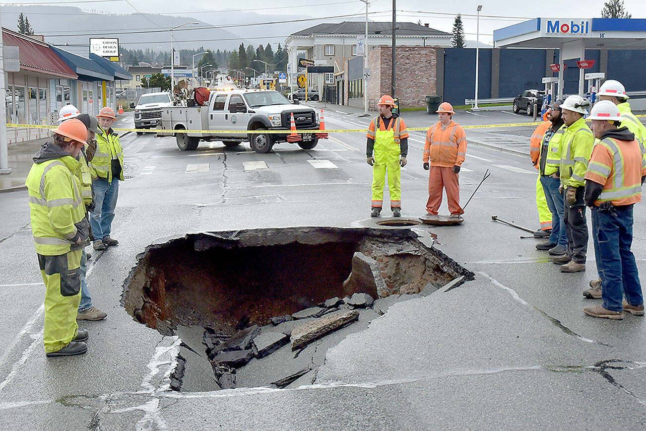 Port Angeles Public Works and Washington State Department of Transportation officials examine a sinkhole in the middle of Fifth and Lincoln streets in Port Angeles on Wednesday after water from a broken water main tore up the pavement. (Keith Thorpe/Peninsula Daily News)