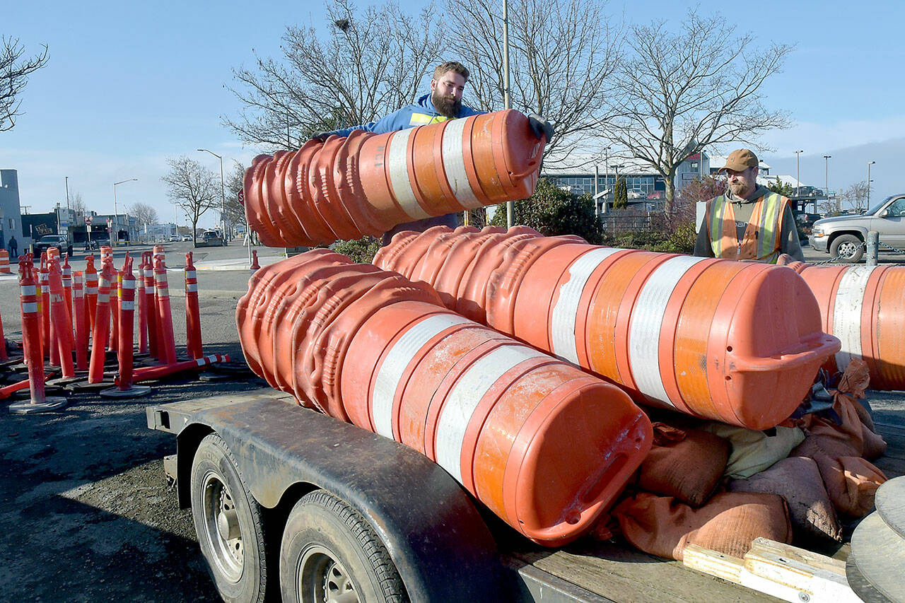 Chris Johnson of Nordland-based Nordland Construction loads traffic drums onto a trailer as coworker Robert Bufford prepares to secure the load as the pair prepares to open the parking lot at Port Angeles City Pier to automobiles on Friday. The work was part of a project to improve storm drainage, replace damaged sidewalks and ADA ramps and mitigate shoreline erosion around the lot, which had been closed since early January. Tree replacement and other project detail work is expected to follow over the next few weeks. (KEITH THORPE/PENINSULA DAILY NEWS)