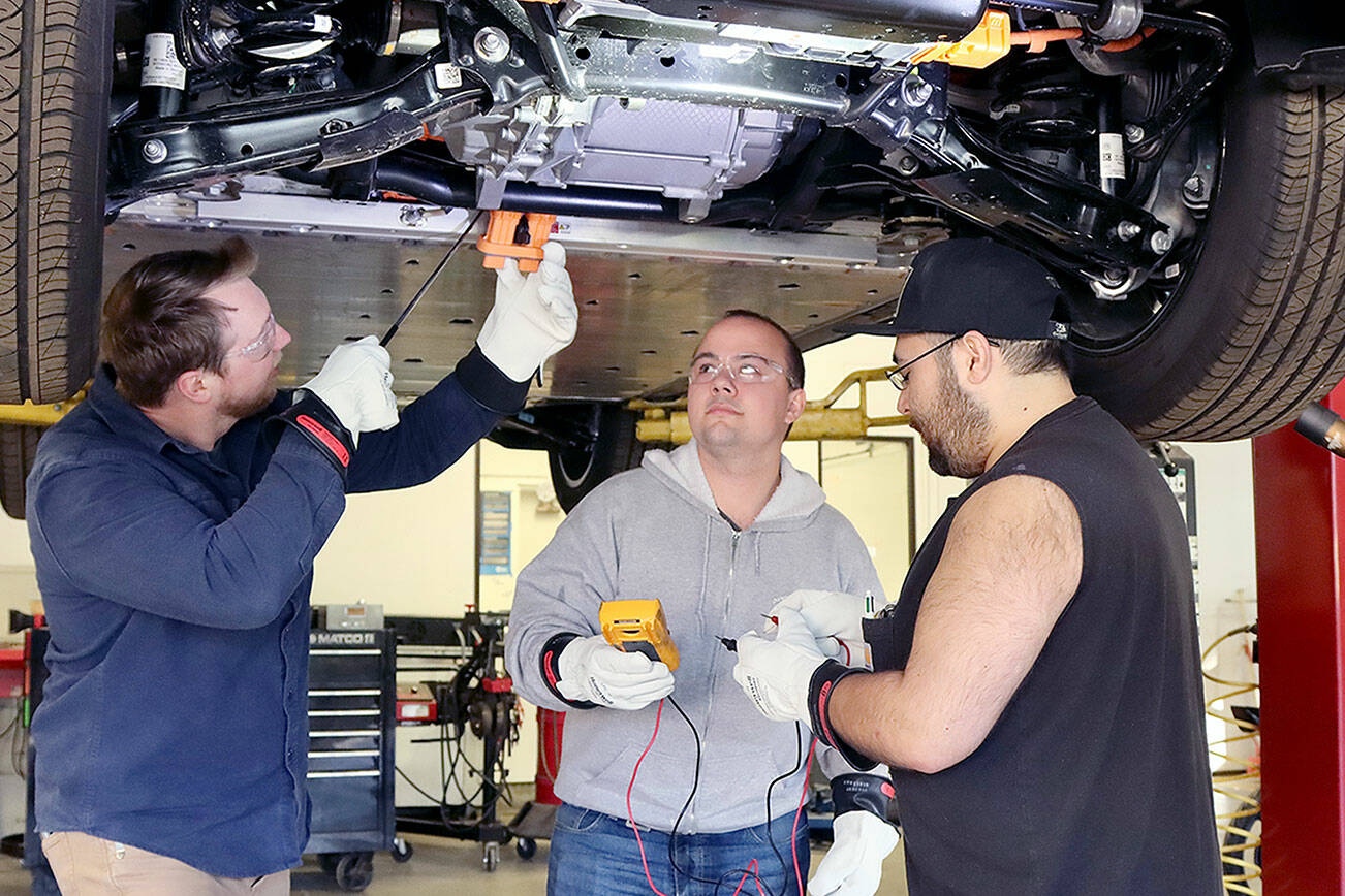 Instructor Josh Taylor, left, points out the workings of an electric vehicle on Wednesday at the Auto Technology Certification Program at Peninsula College. Nick Schommer, center, and Brian Selk get ready to do some testing on the electric auto’s parts from underneath the vehicle. (Dave Logan/for Peninsula Daily News)