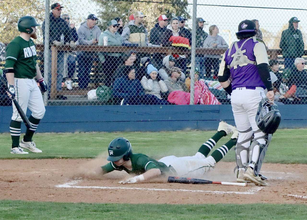 Port Angeles’ Alex Angevine slides home safely against Sequim as catcher Ayden Holland waits for a throw. In the on-deck circle is Port Angeles’ Ezra Townsend. (Dave Logan/for Peninsula Daily News)