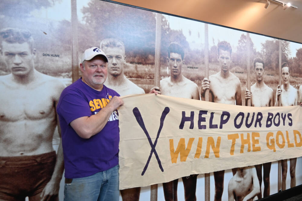 Randy Perry and Judy Reandeau Stipe, volunteer executive director of Sequim Museum & Arts, hold aloft a banner from "The Boys in the Boat" film Perry purchased and is loaning to the museum. (Michael Dashiell/Olympic Peninsula News Group)