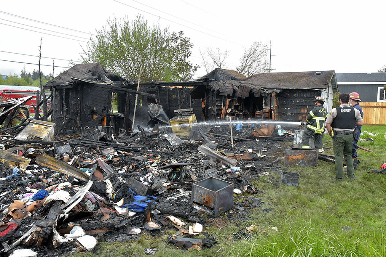Clallam County Fire District Captain Marty Martinez sprays water on a hot spot of a fire that destroyed a house and adjoining RV in the 700 block of East Kemp Street near Port Angeles on Friday morning. (Keith Thorpe/Peninsula Daily News)