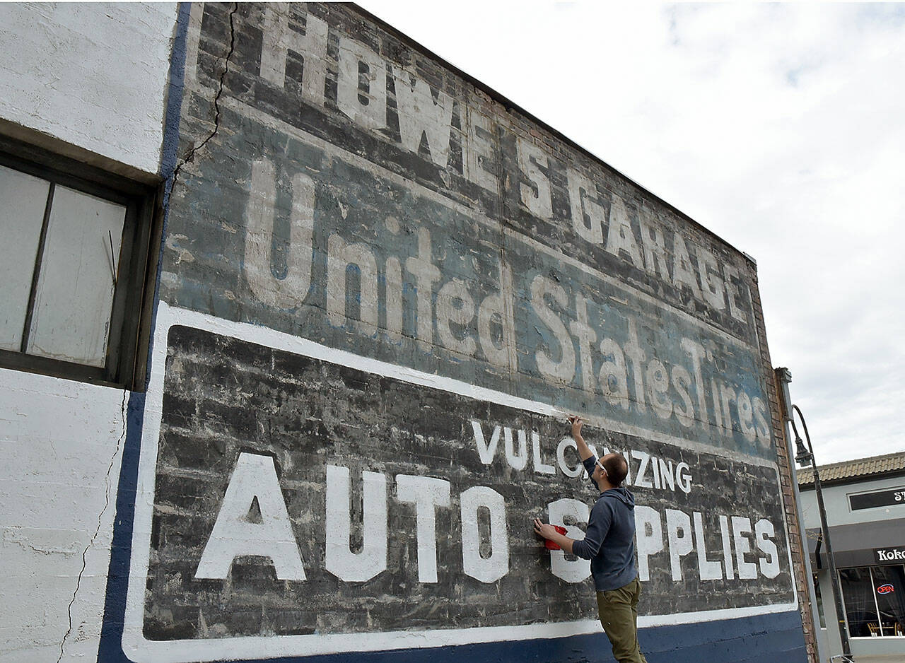 Kyle Zimmerman, co-owner of The Hub at Front and Lincoln streets in downtown Port Angeles, adds a new coat of paint on Wednesday to an advertising sign on the back of his building that was uncovered during the demolition of a derelict building that once hid the sign from view. Zimmerman said The Hub, formerly Mathews Glass and Howe's Garage before that, is being converted to an artist's workspace and entertainment venue with an opening set for late May or early June. Although The Hub will have no control over any new construction that might later hide the automotive signs, Zimmerman said restoring the paint is an interesting addition to the downtown area for as long as it lasts. (Keith Thorpe/Peninsula Daily News)