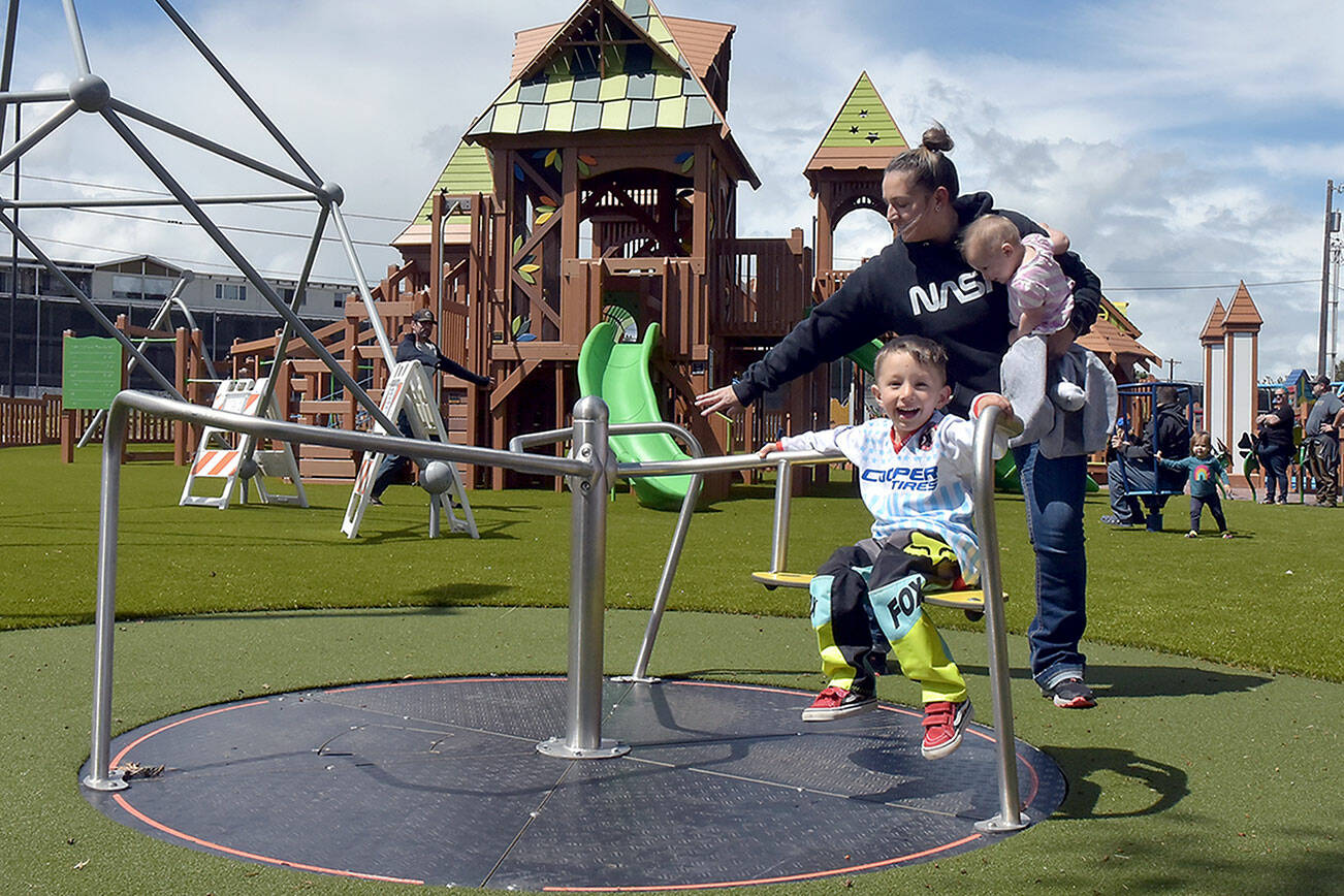 KEITH THORPE/PENINSULA DAILY NEWS
Three-year-old Archie Hanson takes a spin on a merry-go-round pushed by his mother, Justine Hanson of Port Angeles, with sister Arlene Hanson 7 months, during Sunday's grand reopening of the Dream Playground at Erickson Playfield in Port Angeles. The playground was rebuilt earlier this month by volunteers after an arson fire destroyed much of the playground equipment in December. Although there are still details to attend to and minor adjustments to be made, the facility will be open daily from dawn until dusk.