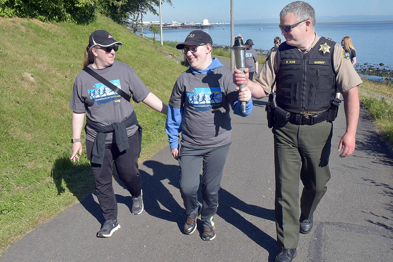 Clallam County Sheriff Brian King, right, carries a ceremonial torch with Special Olympian William Sirguy, center, accompanied by his mother, Katie Sirguy, during Friday’s Special Olympics Law Enforcement Torch Run along the Waterfront Trail in Port Angeles. The event, designed to raise awareness and funds for the Special Olympics movement, brought together law enforcement officers from Clallam, Jefferson and Kitsap counties for a march across the North Olympic Peninsula. (Keith Thorpe/Peninsula Daily News)