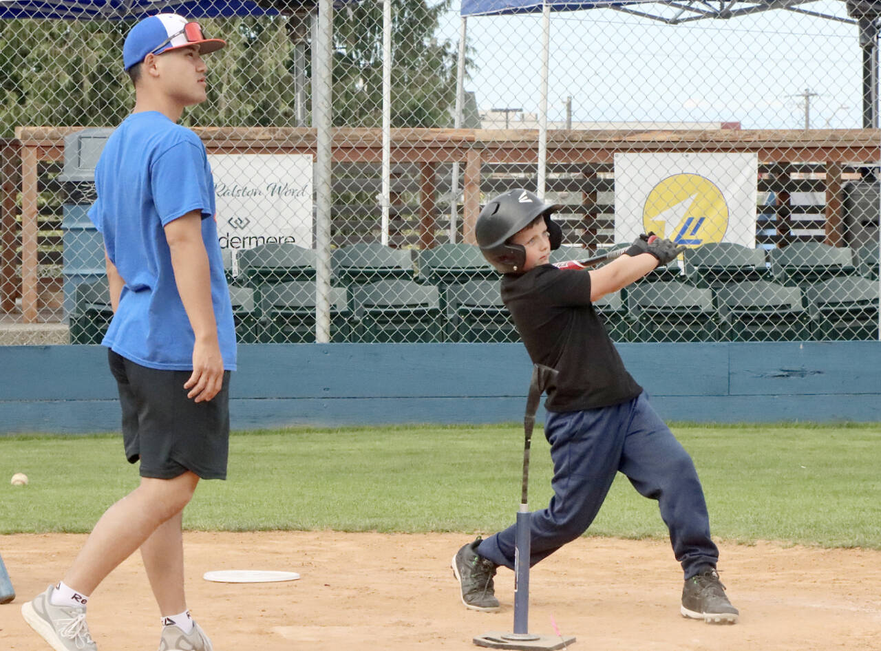 A pitch, hit and run competition was held Monday at Civic Field in Port Angeles hosted by the Port Angeles Lefties. More than 50 kids from 7 to 14 years old, some from as far away as Seattle, competed for prizes and a chance to advance to state and regional competitions. Here, Jackson Carmichael, 8, of Port Angeles takes a mighty swing off a tee as Port Angeles Leftie Kosei Suzuki assists. (Dave Logan/for Peninsula Daily News)