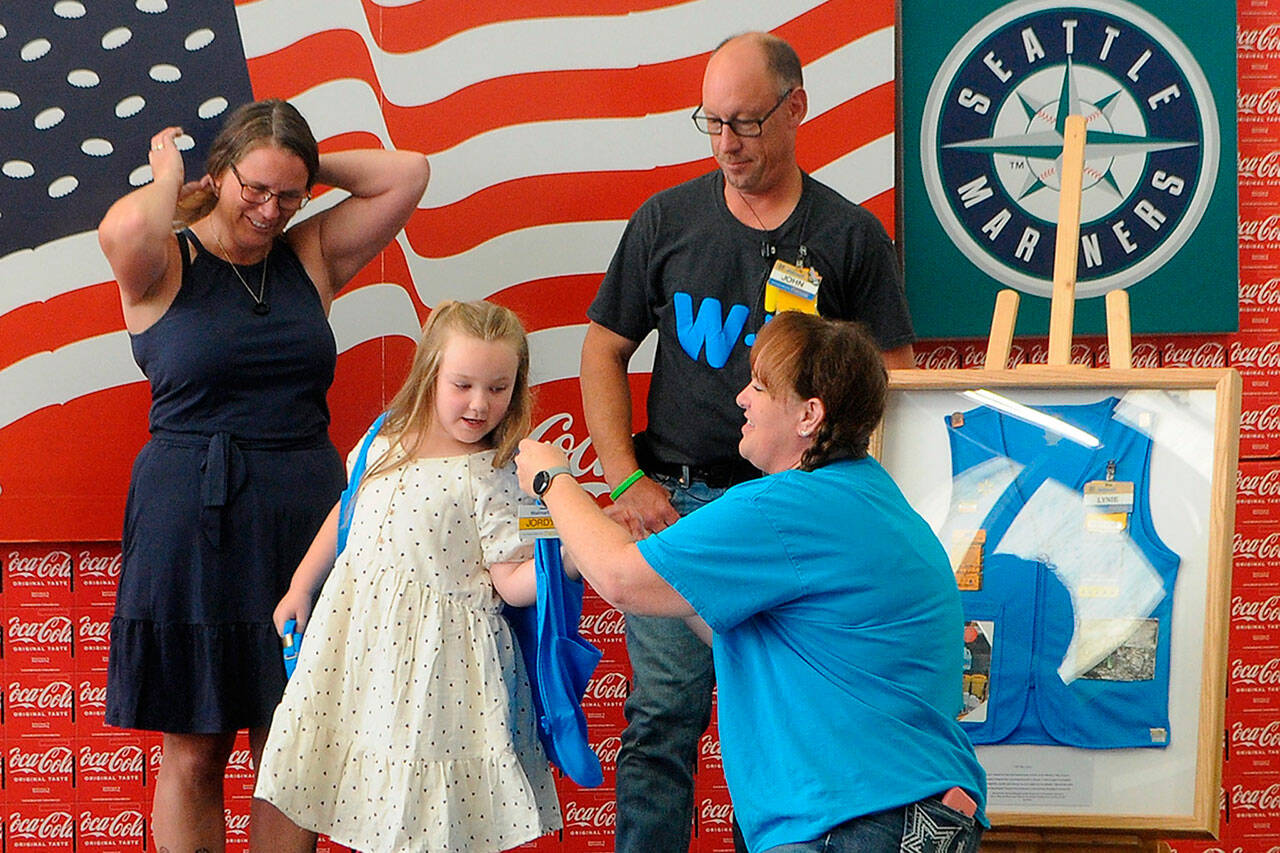 Jessica Davis helps Jordyn Mancuso-Staus put on a personalized vest during a ribbon cutting for the remodel of the Sequim Walmart as Jordyn's grandmother Donna Staus, left, and Jessica's husband John-Paul Davis watch. The Davises presented Donna with a shadowbox with her late-husband Lynie Staus' work vest. He died May 1 shortly before his 24th anniversary with the company. (Matthew Nash/Olympic Peninsula News Group)