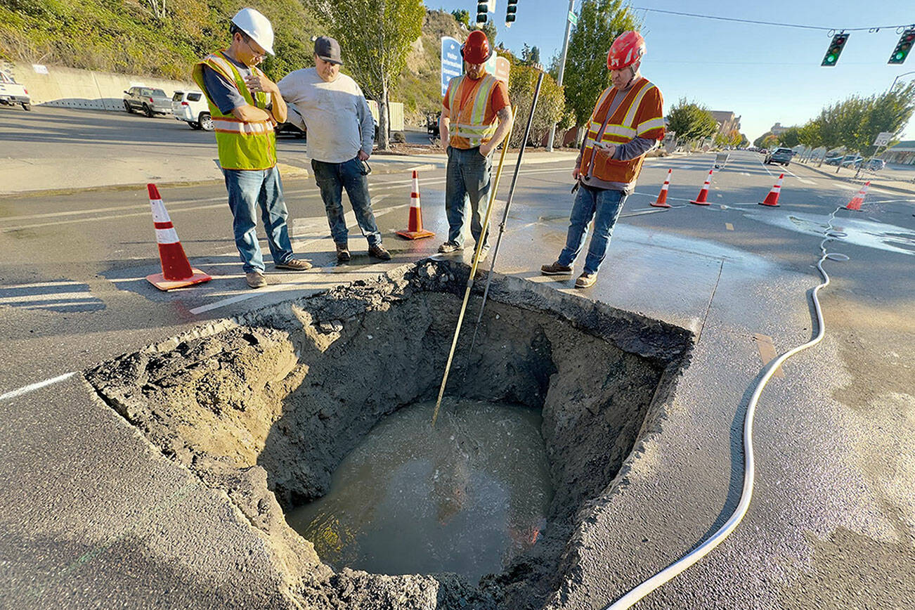 Port Townsend Public Works Director Steve King, left, discusses ways to repair the broken sewer line that developed a sinkhole late Friday night on Water Street at the entrance to the Port Townsend ferry dock, with Talon Cameron of Seaton Construction, Lane Dodson and Adam Fructas. Raw sewage continues to flow through the 70-year-old pipe and partially fills the hole. Plans were to make a temporary fix with a steel plate over the hole until more permanent repairs could be made. (Steve Mullensky/For Peninsula Daily News)