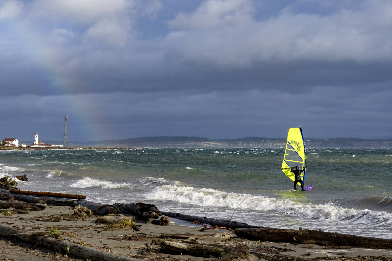 A kiteboarder takes his board into the storm-tossed waters of Port Townsend Bay at Fort Worden State Park during a sunbreak on Saturday, while a rainbow forms over the Point Wilson Lighthouse. (Steve Mullensky/for Peninsula Daily News)