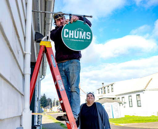 Connor Cunningham of Port Townsend, an employee of the Port of Port Townsend, hangs a sign for new business owner Lori Hanemann of Port Townsend on Friday at her shop in what was a former moorage office at Point Hudson Marina. (Steve Mullensky/for Peninsula Daily News)