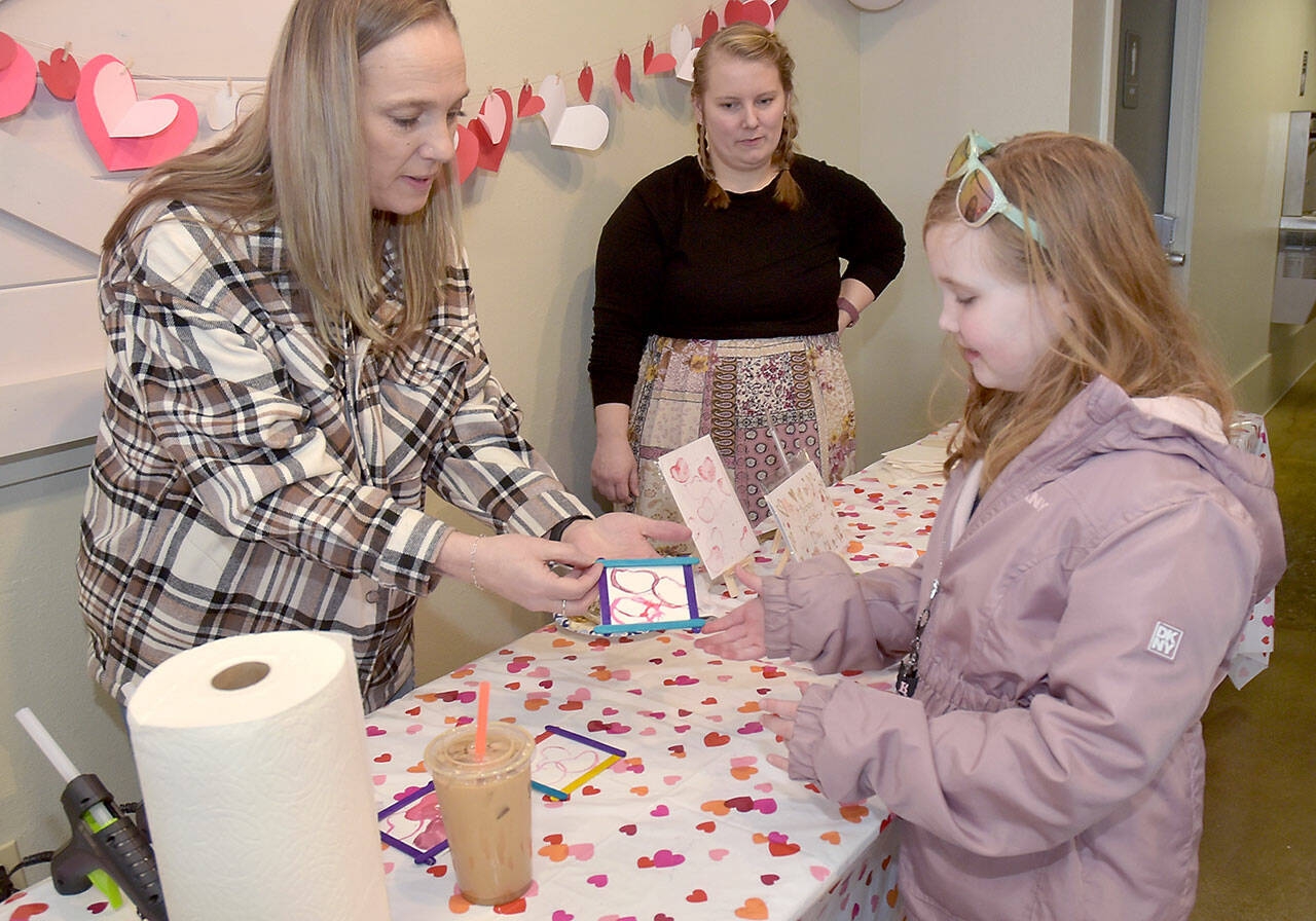 Madison Canterbury, 7, of Shelton looks at a Valentine’s gift she created with the assistance of volunteers Chandra McGuff, left, and Nicole Lemon at a craft table set up outside the Silver Lining Cafe at The Wharf on Saturday on the Port Angeles waterfront. Youngsters were given the opportunity to create gifts and Valentine’s cookies during the event. (Keith Thorpe/Peninsula Daily News)