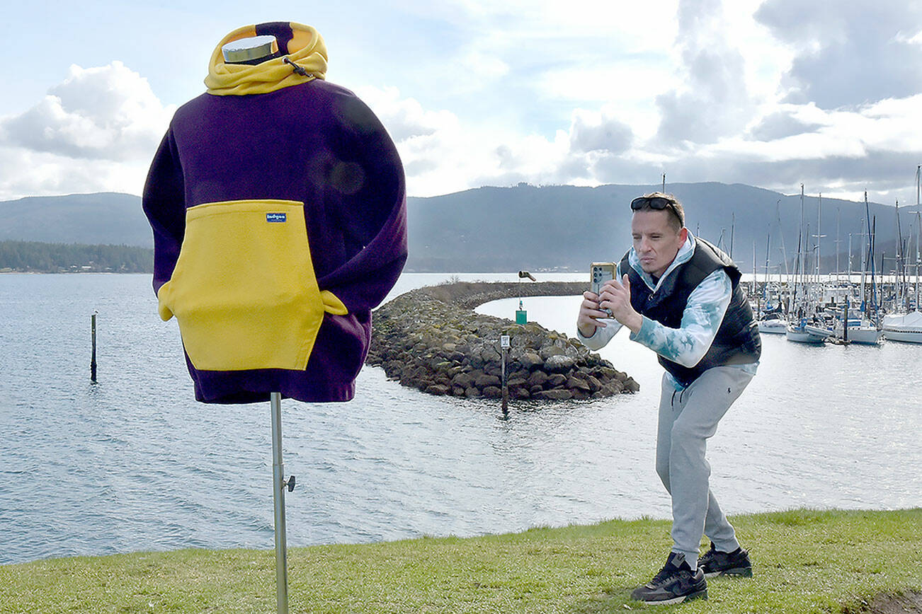 Joseph Prince takes a photo of a hoodie jacket on Wednesday on a small hill overlooking the entrance to John Wayne Marina near Sequim. Prince, a member of the Jamestown S’Klallam Tribe, said the weather was ideal for adding items to the catalog of his online vintage clothing business. (Keith Thorpe/Peninsula Daily News)