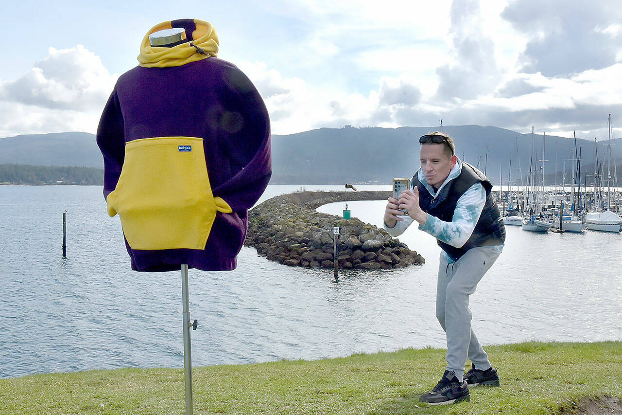 Joseph Prince takes a photo of a hoodie jacket on Wednesday on a small hill overlooking the entrance to John Wayne Marina near Sequim. Prince, a member of the Jamestown S’Klallam Tribe, said the weather was ideal for adding items to the catalog of his online vintage clothing business. (Keith Thorpe/Peninsula Daily News)