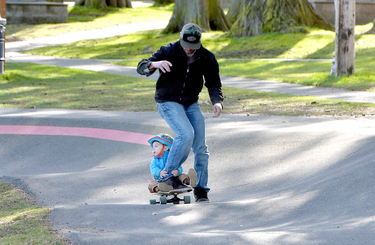 Lucas Niclas, 23 months, hangs onto to the leg of his father, Ben Niclas of Sequim, as they make their way around the pump track on Friday at Erickson Playfield in Port Angeles. The pair were on a family outing to the popular attraction. (Keith Thorpe/Peninsula Daily News)