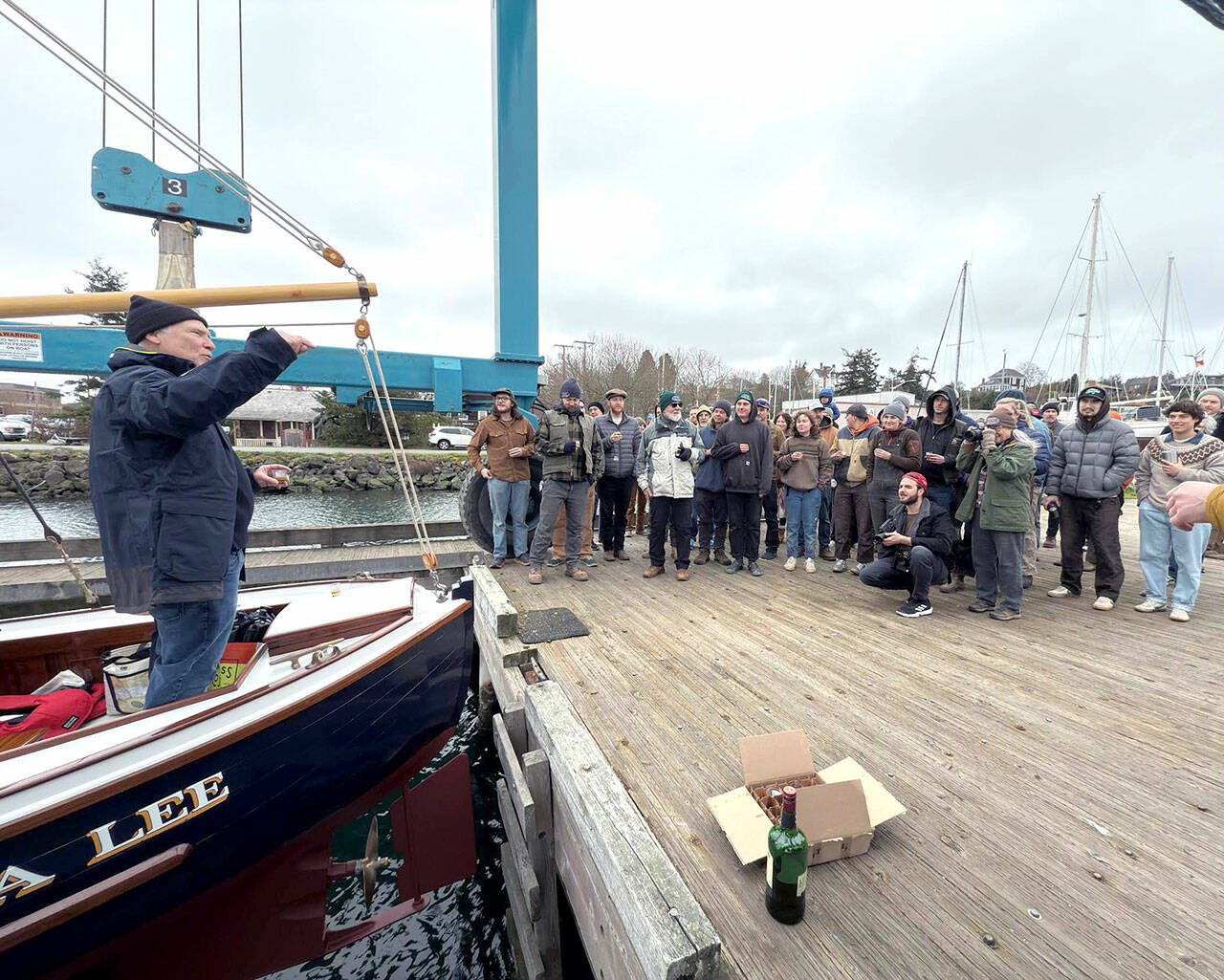 Chuck Hancock of Tacoma raises a glass to toast the launching of his boat, Diana Lee, named after his wife, which was built by the students of the Northwest School of Wooden Boat Building in Port Hadlock. The boat is a 24-foot one-off design by designer Jonathan Madison of Lummi Island and was trailered in and launched from the travel lift at Point Hudson Marina on Friday morning. (Steve Mullensky/for Peninsula Daily News)