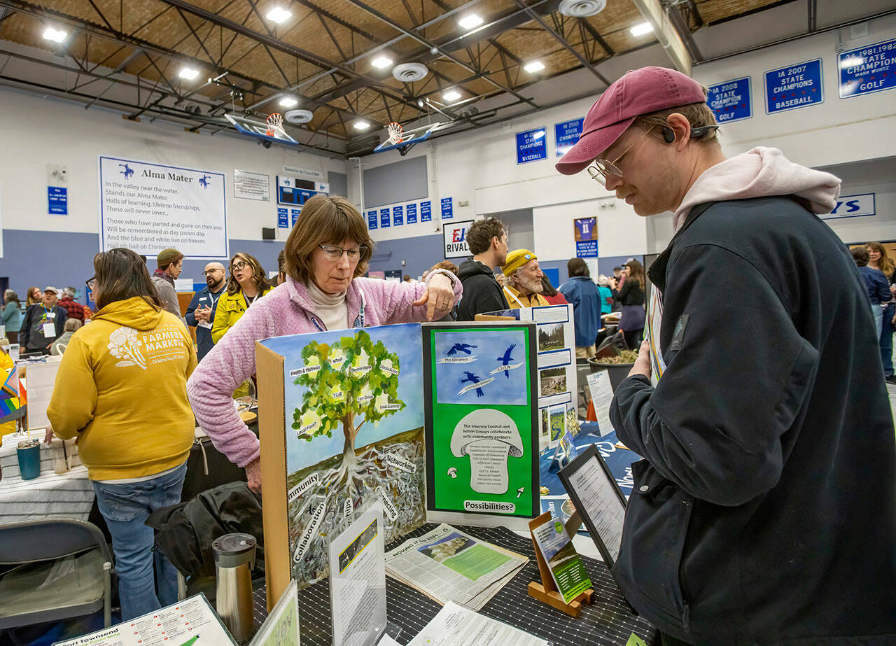 Cindy Taylor of Port Townsend, representing the environmental group Local 20/20, points to printed information available about the organization to an interested party while at the Jefferson County Connectivity Summit at Chimacum High School on Saturday. (Steve Mullensky/for Peninsula Daily News)