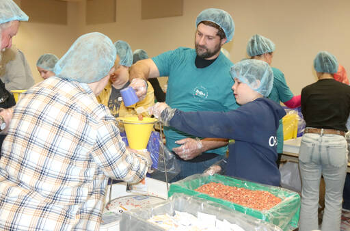Levi Oravetz, 9, and his father Adam Oravetz put pre-measured rice and lentils into a funnel to be packaged for families in Ecuador. More than 100 volunteers from Independent Bible Church of Port Angeles packed 65,000 meals on Saturday. Almost $23,000 was raised by the church to buy the supplies. (Dave Logan/for Peninsula Daily News)