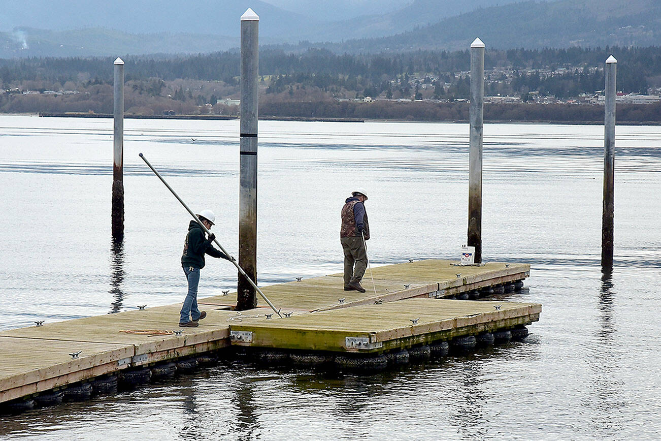 Port Angeles Parks & Recreation Department workers Brooke Keohokaloke, left, and Brian Flores steer a section of floating dock into place at the boat launch on Ediz Hook in Port Angeles on Wednesday. The floats had been removed and stored in a safe location to prevent wave damage from winter storms. (Keith Thorpe/Peninsula Daily News)