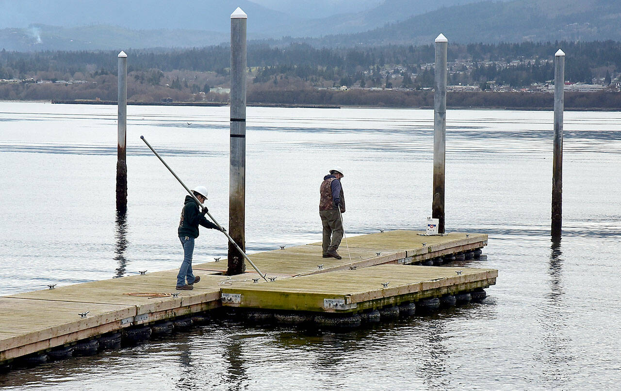 Port Angeles Parks & Recreation Department workers Brooke Keohokaloke, left, and Brian Flores steer a section of floating dock into place at the boat launch on Ediz Hook in Port Angeles on Wednesday. The floats had been removed and stored in a safe location to prevent wave damage from winter storms. (Keith Thorpe/Peninsula Daily News)