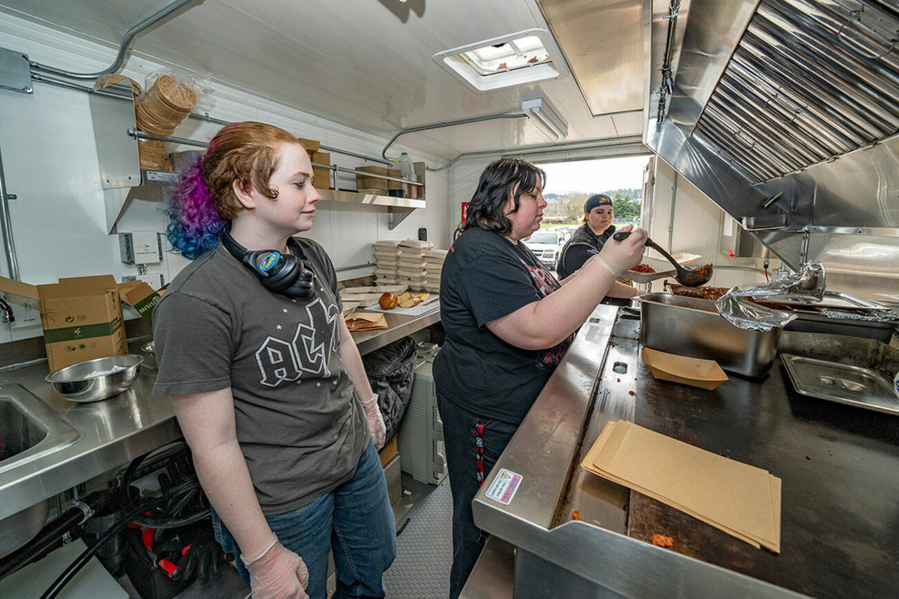 Steve Mullensky/for Peninsula Daily News
Port Townsend High School culinary arts student Jasper Ziese, left, watches as fellow students Emil Brown sauces the dish and Raivyn Johnson, right, waits to box it up. The students prepared and served a free lunch from the program's food truck, Culinary Cruiser, for a senior project on Saturday.